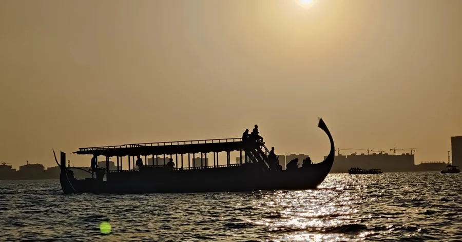A traditional dhoni boat silhouetted on calm water at sunset