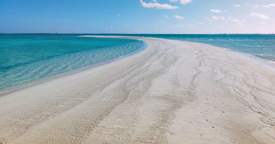 A long curving white sandbank in a shallow turquoise lagoon